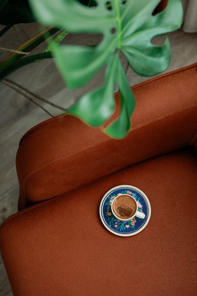 A beautifully designed coffee cup sits on a brown sofa with rich leaf decor, creating a cozy and inviting ambiance.