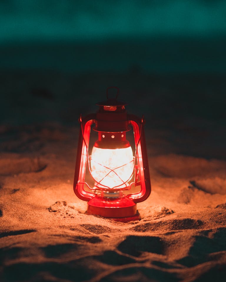 A glowing red lantern lights up the sandy beach during nighttime, creating a warm, cozy atmosphere.