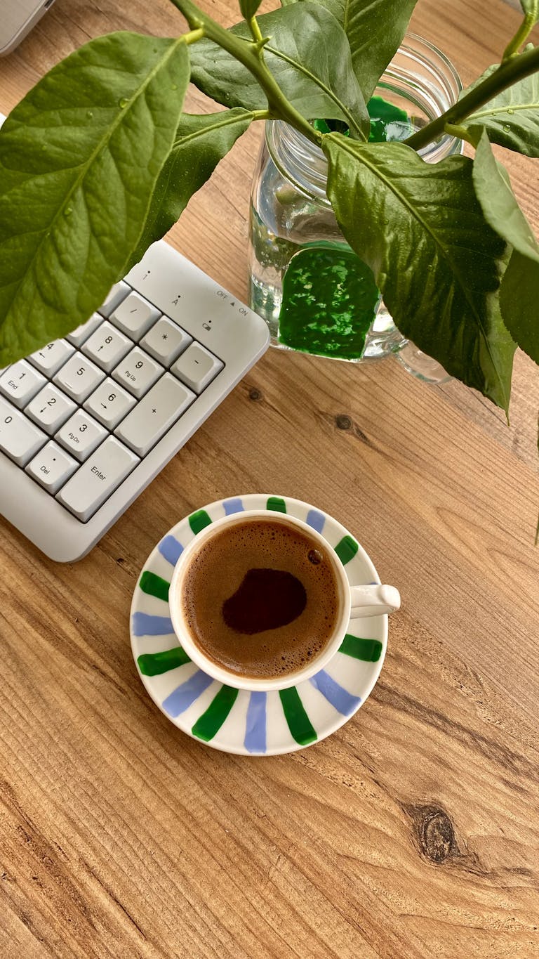 A warm, inviting workspace featuring a cup of coffee, a keyboard, and lush green leaves.