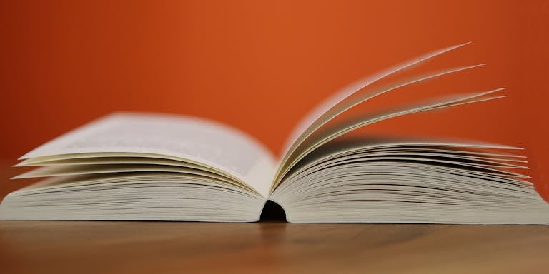 An open book with pages turning against a vibrant orange background, symbolizing knowledge and education.