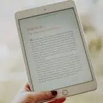 Close-up of a hand holding a tablet displaying an e-book page.