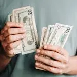 Close-up of a person counting US dollar bills indoors. Financial concept.
