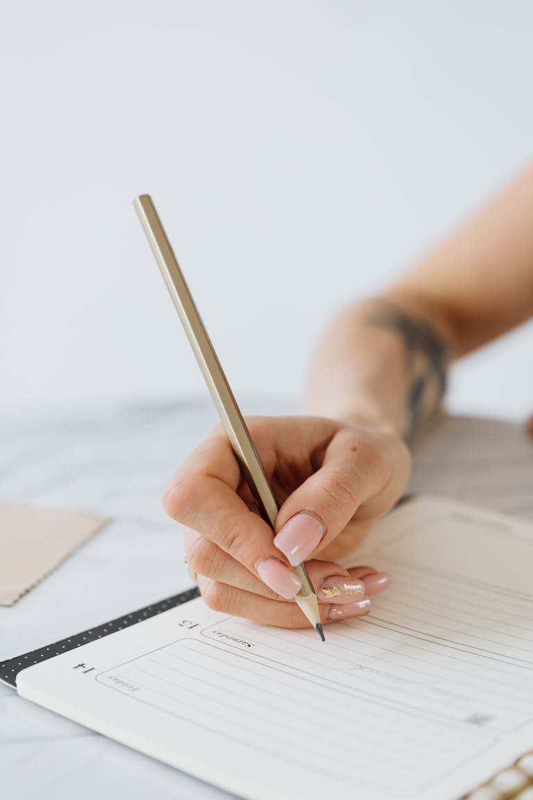 Close-up of a woman's hand writing in a notepad with a pencil.
