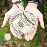 Hands holding crumpled money outdoors, symbolizing charity and financial support.