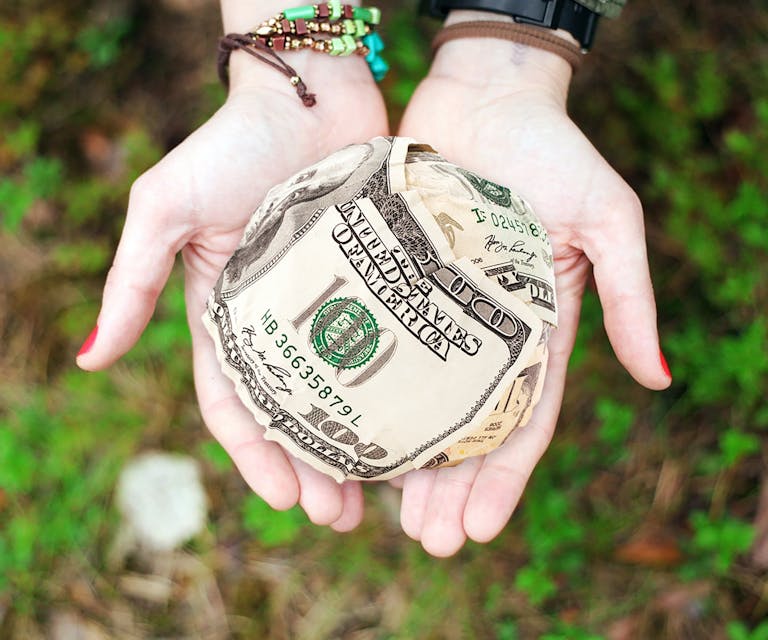 Hands holding crumpled money outdoors, symbolizing charity and financial support.
