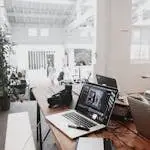 A bright, modern workspace featuring laptops, a camera, and a drawing tablet in an indoor office.