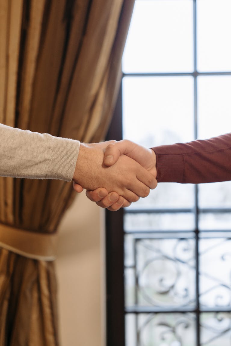 A close-up of two adults shaking hands indoors beside a window.