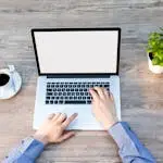 A comforting workspace with a laptop, coffee cup, and potted plant on a wooden desk.