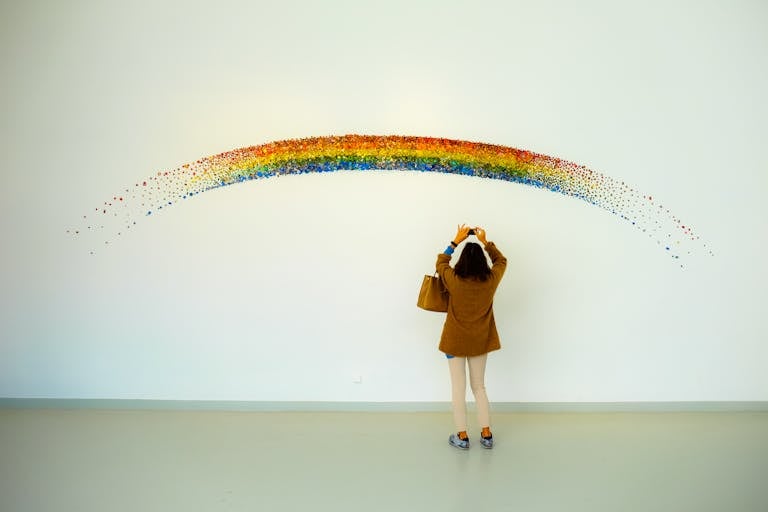 A woman stands observing a colorful rainbow art installation indoors.