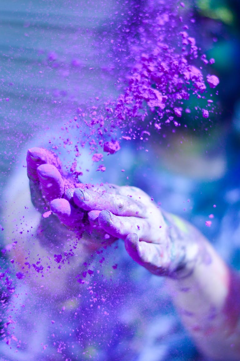 Close-up of hands throwing vibrant purple powder outdoors, capturing motion and color.