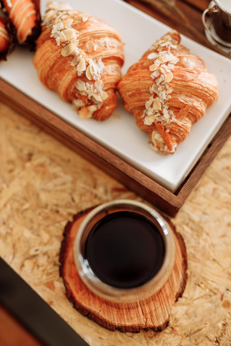 Fresh almond croissants served with coffee on a rustic wooden table.