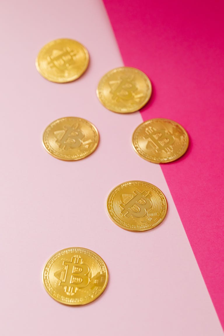 Golden Bitcoin coins placed on a stylish pink gradient background, symbolizing modern cryptocurrency.