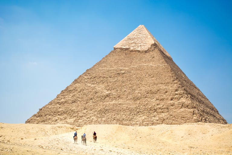 Iconic Giza Pyramid with riders on camels under bright daylight, capturing Egyptian desert landscapes.
