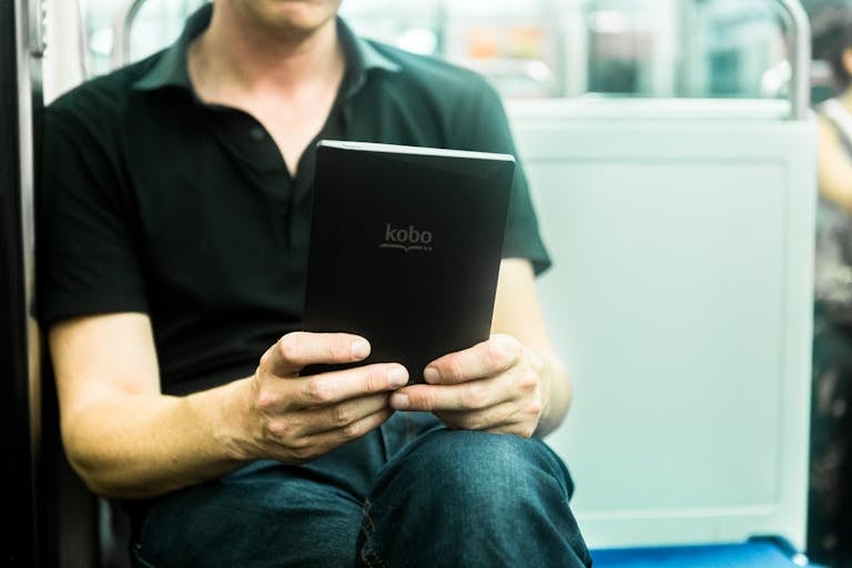Man engrossed in reading on a Kobo e-reader while traveling on the Paris subway.