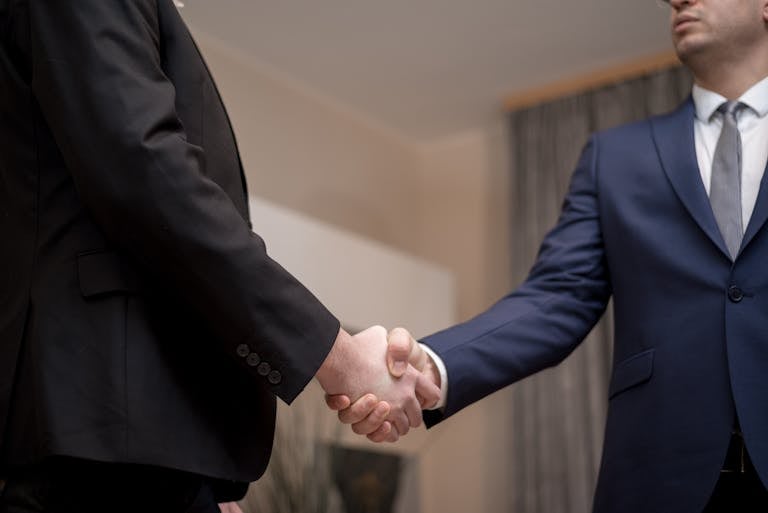 Two businessmen in suits shaking hands, emphasizing trust and partnership indoors.