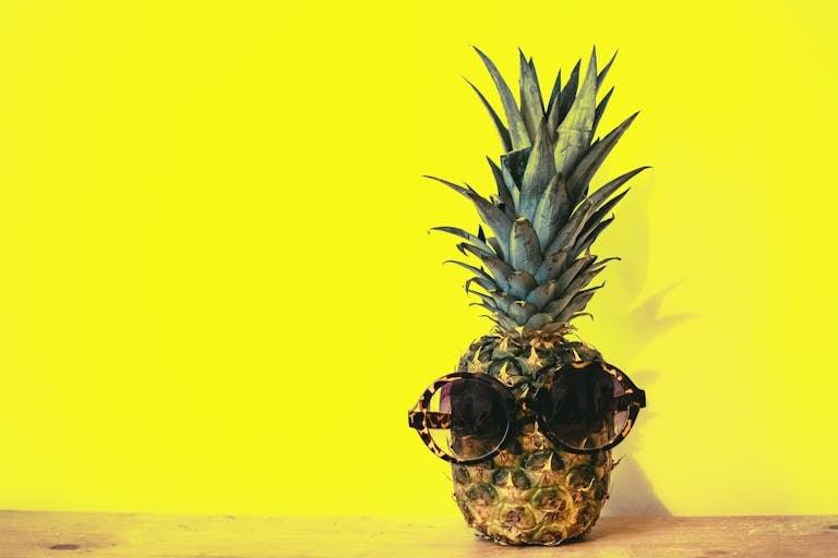 A stylish pineapple wearing sunglasses against a bright yellow background.