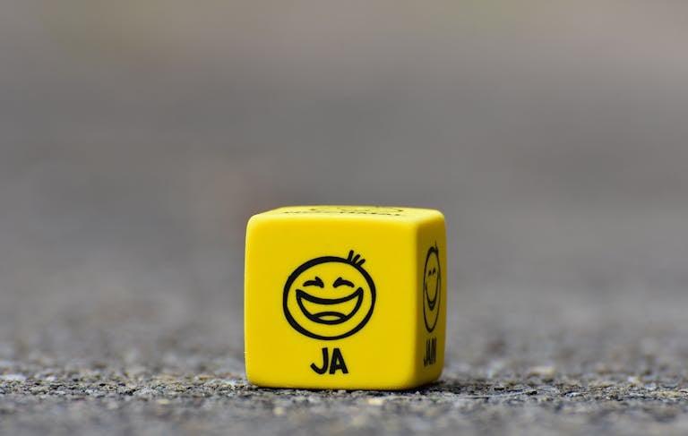 Close-up of a yellow dice featuring a smiley face emoticon symbolizing happiness and fun.