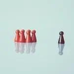 Red game pieces grouped with one isolated piece symbolizing social distancing on a reflective surface.