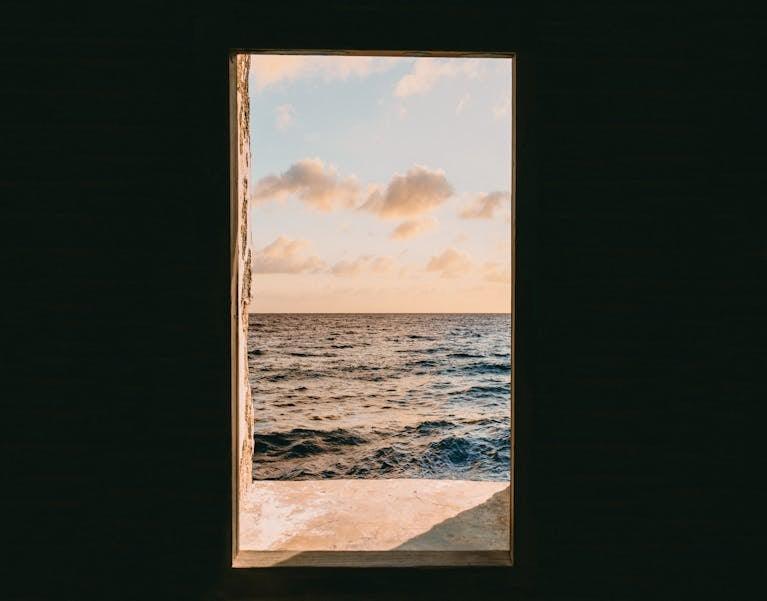 Tranquil ocean view framed by an open doorway at sunset, showcasing nature's simplicity.