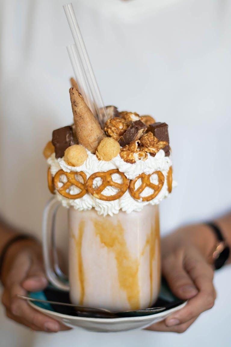 A delectable dessert milkshake adorned with pretzels, whipped cream, and various toppings.