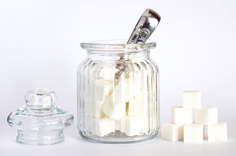 Close-up of a glass jar filled with sugar cubes on a white background. Minimalist stock photo.