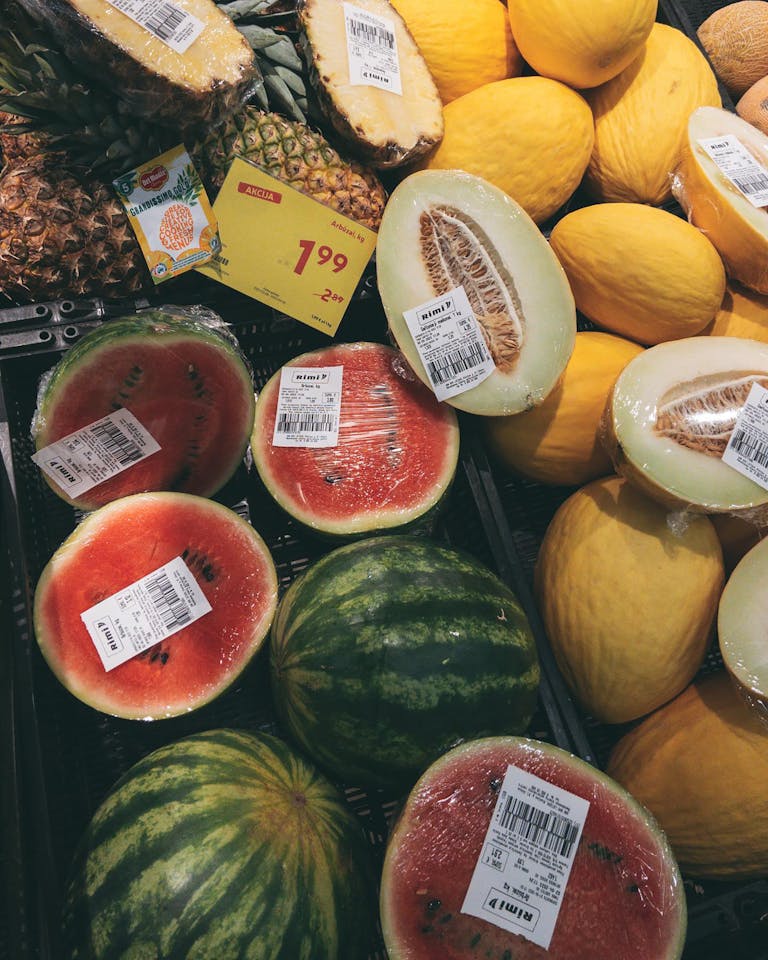 Colorful display of melons, watermelons, and pineapples on sale at a grocery store.